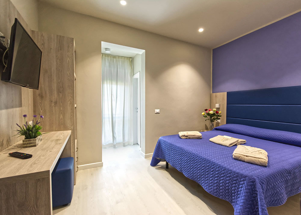 Pironi-Lab-Ingresso_ Camera vistamare suite, letto matrimoniale con copriletto blu e portafinesta con vista sul mare