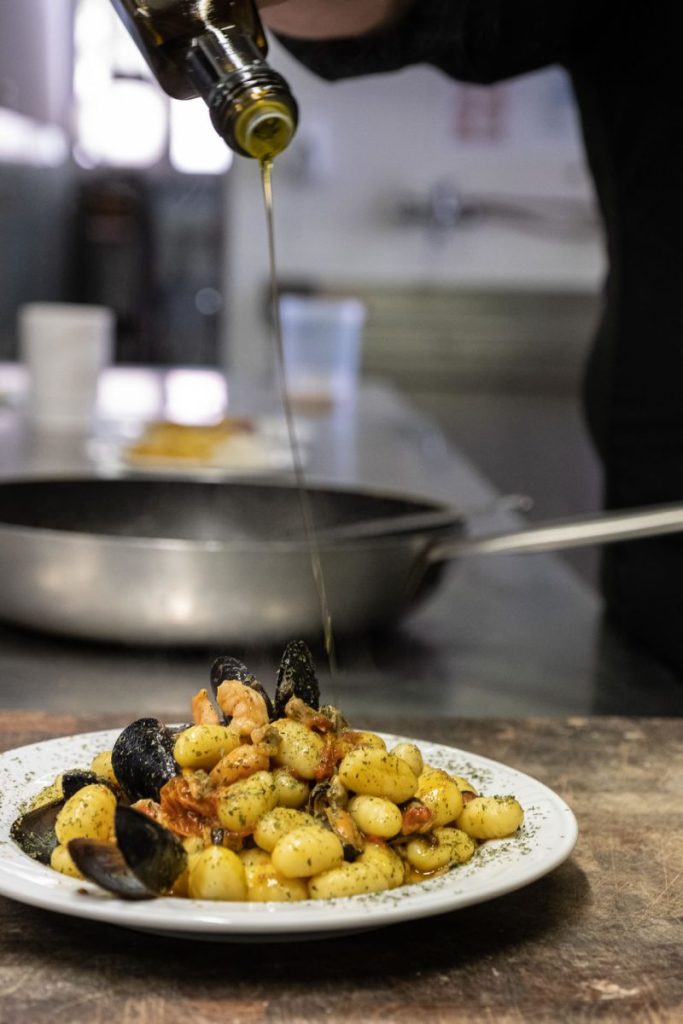 Chef aggiunge un filo d'olio al piatto di gnocchi alle vongole